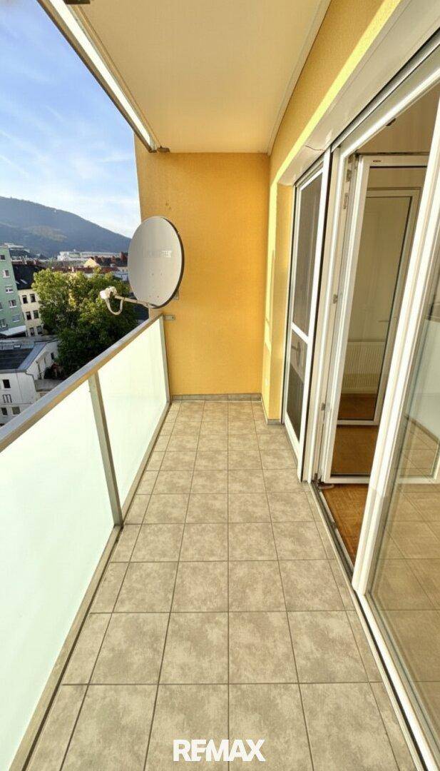 Schmaler Balkon mit Fliesenboden und Satellitenschüssel an der gelben Wand.