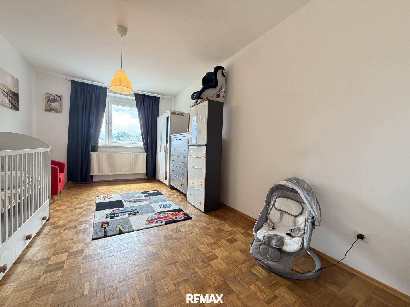Kinderzimmer mit Parkettboden, Babybett und Fenster mit Blick ins Grüne.