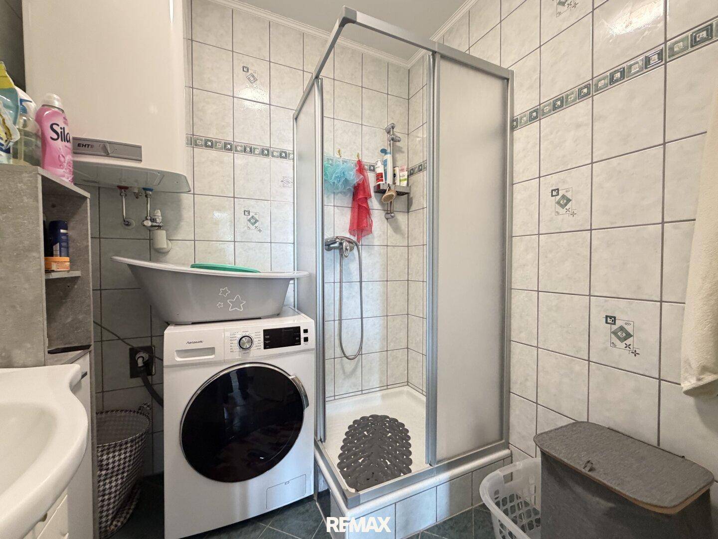 Badezimmer mit Duschkabine, Waschmaschine und gefliesten Wänden.