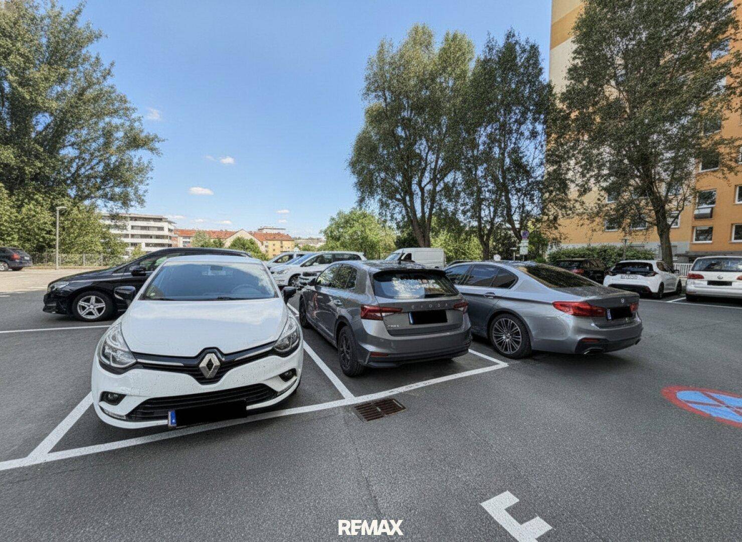 Außenparkplatz mit mehreren Autos und Bäumen an einem sonnigen Tag.