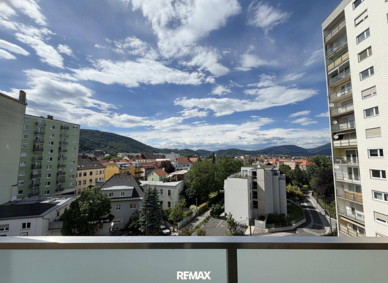Weitblick über die Stadt und die umliegenden Berge von einem Balkon aus.