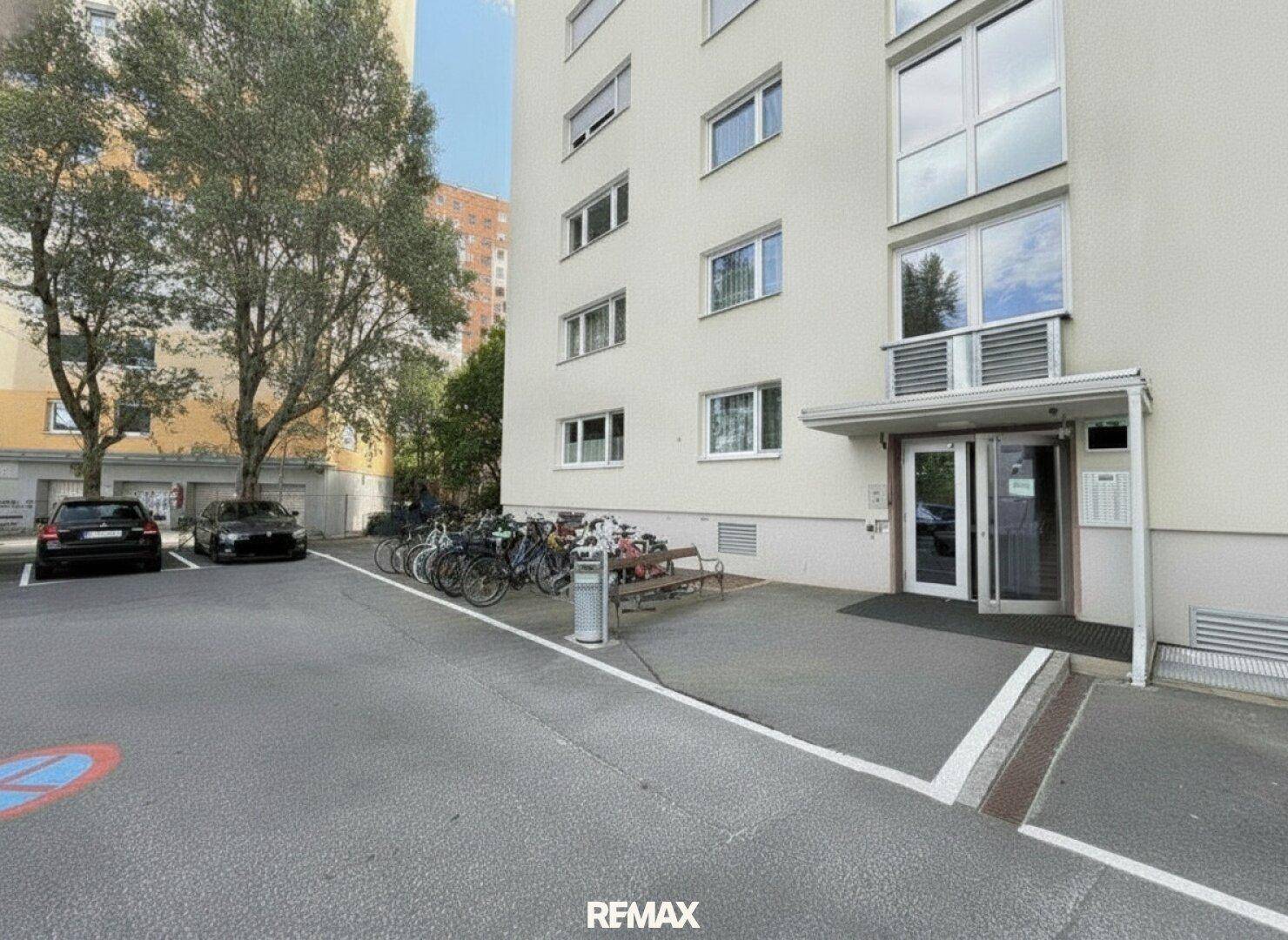 Eingangsbereich eines Mehrfamilienhauses mit Fahrradständern und Parkplätzen.