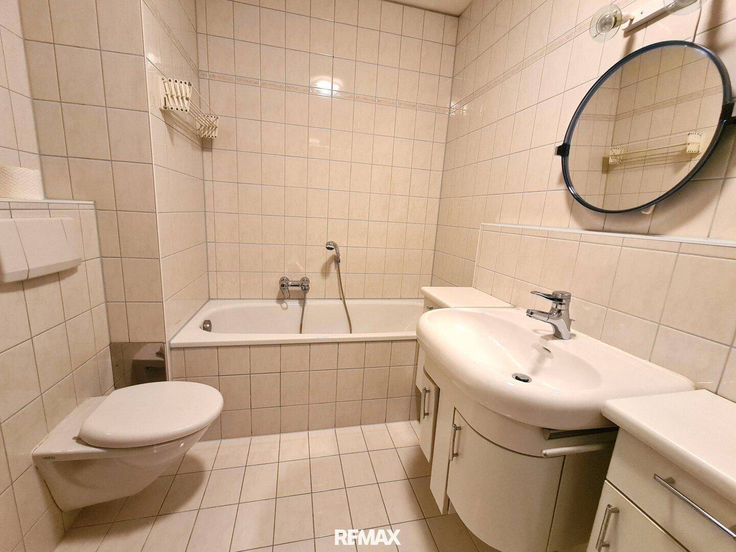 Badezimmer mit beigefarbenen Fliesen, einer Badewanne, Toilette und einem einzelnen Waschbecken.