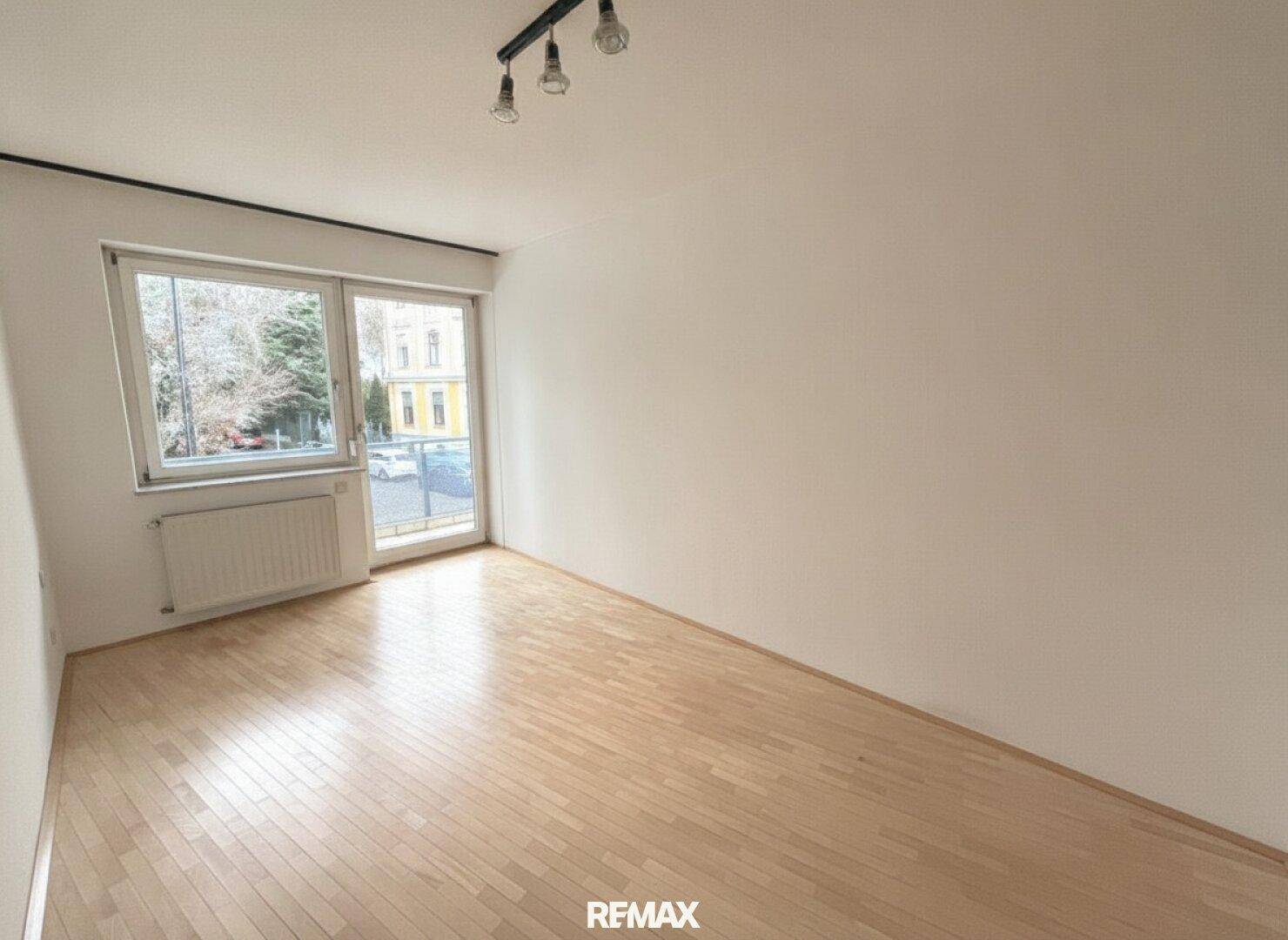 Leeres Schlafzimmer mit Parkettboden, weißen Wänden und direktem Zugang zu einem Außenbereich.