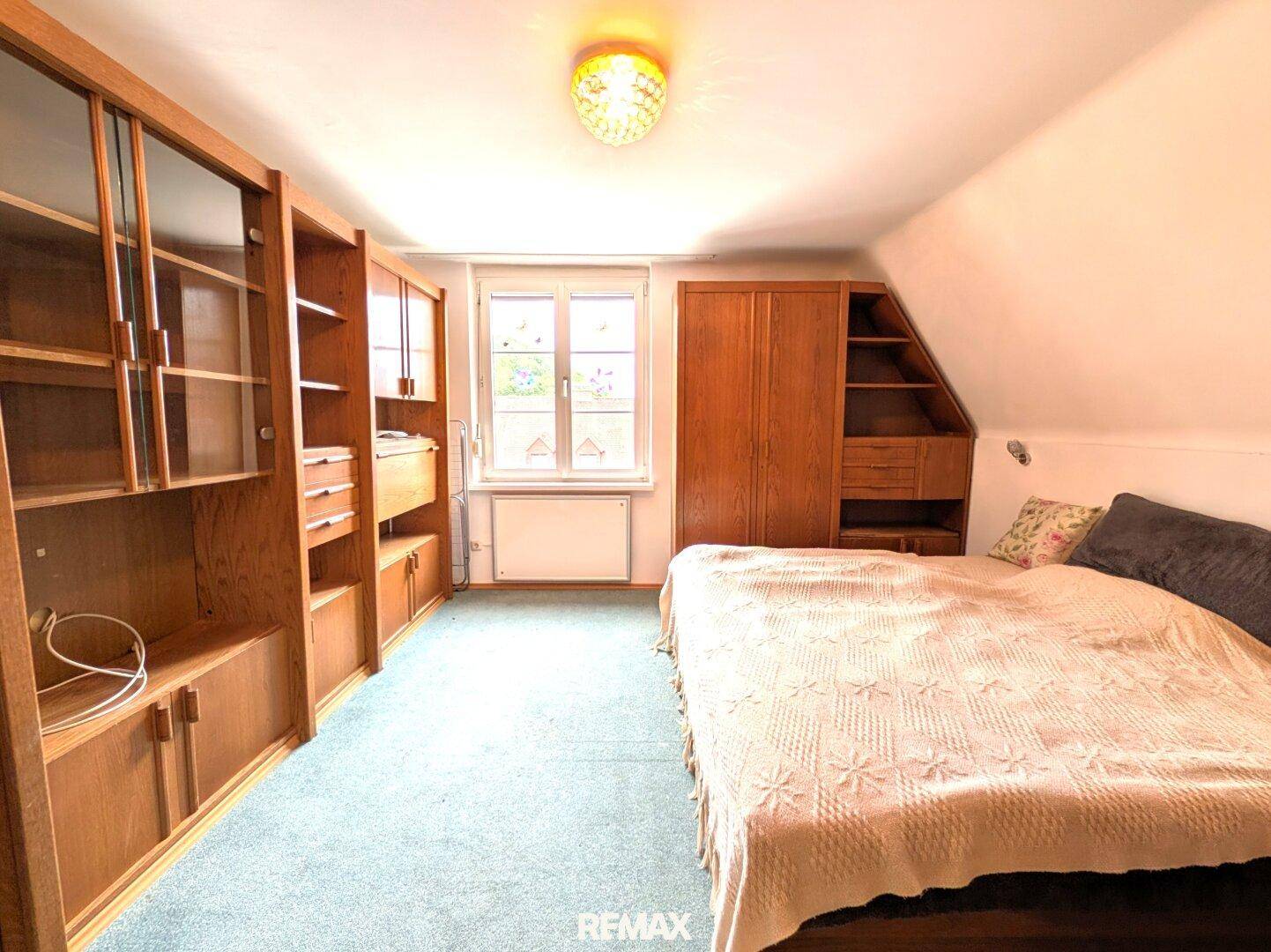 Gemütliches Schlafzimmer mit Teppichboden, Holzmöbeln und Dachschräge, bietet Stauraum.