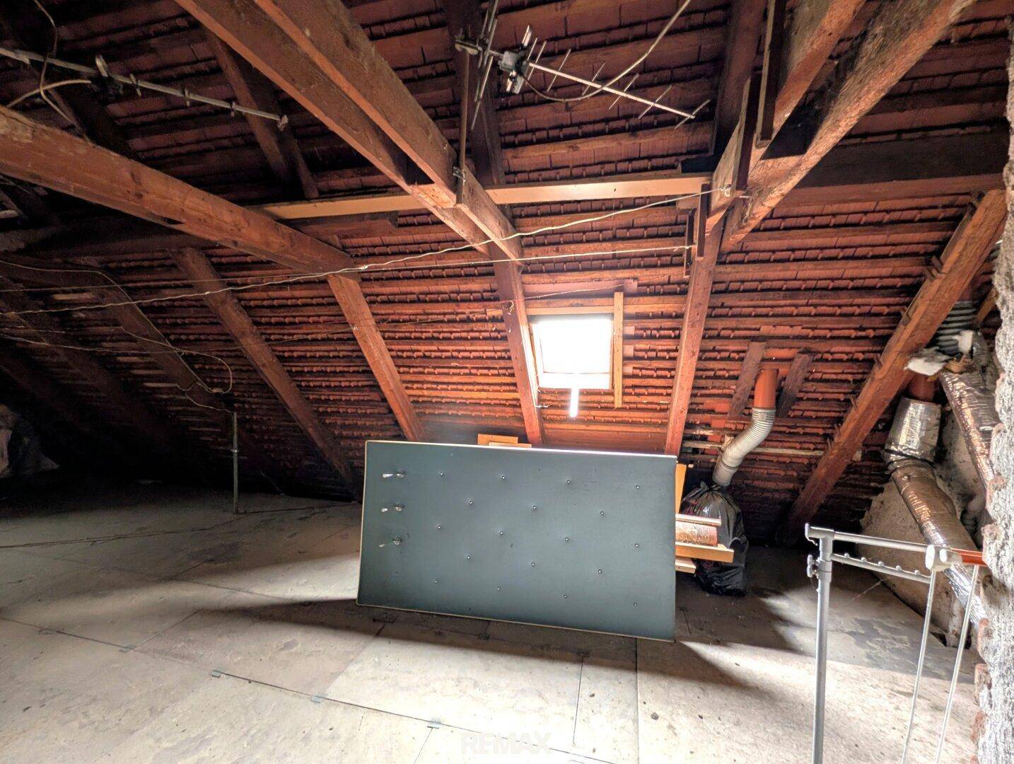 Unausgebauter Dachboden mit sichtbaren Holzbalken und Dachfenster, bietet Stauraum.