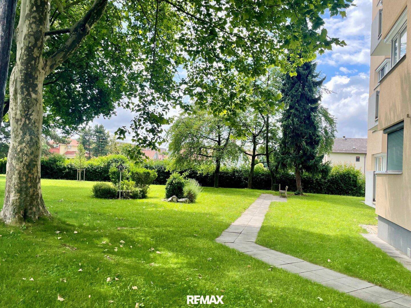 Gepflegter Gemeinschaftsgarten mit Rasenflächen, Bäumen und einem Gehweg.