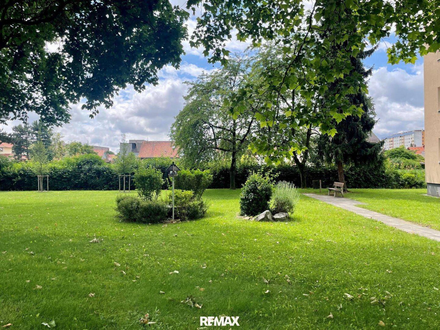 Weitläufiger Gemeinschaftsgarten mit viel Grün, Bäumen und einem Sitzbereich.