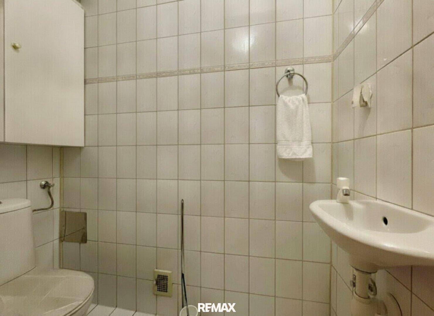 Kleines WC mit Toilette, Waschbecken und weißen Wandfliesen.