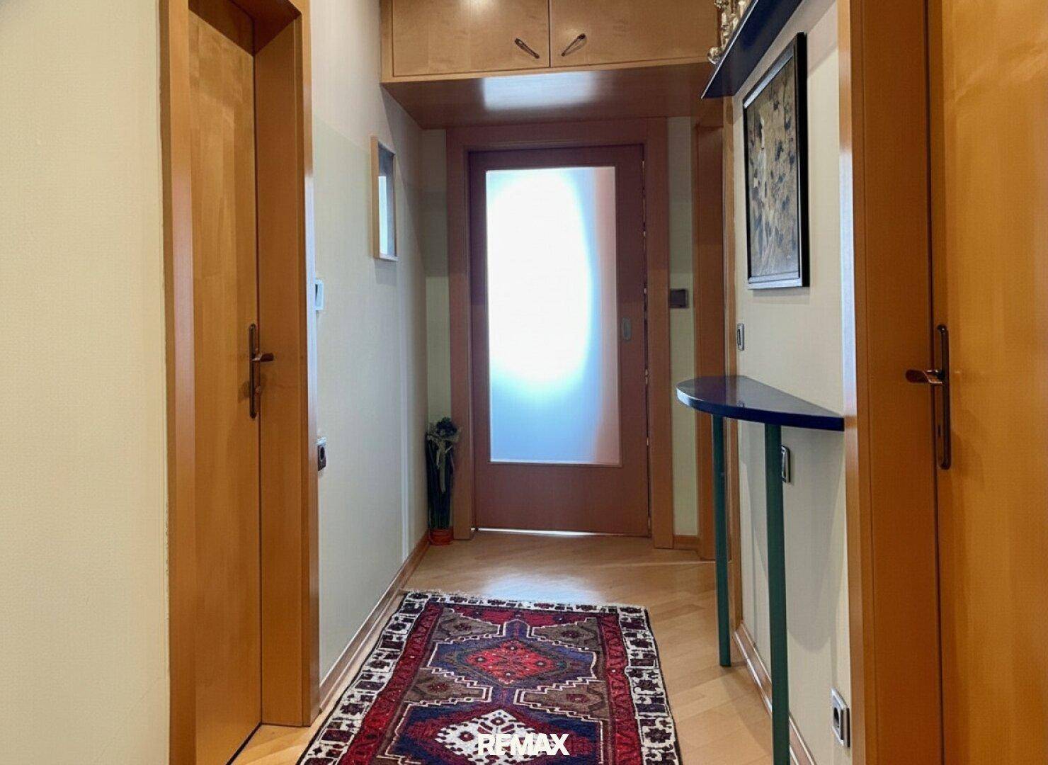 Heller Flur mit Holztüren, Teppich und einem dekorativen Wandregal.