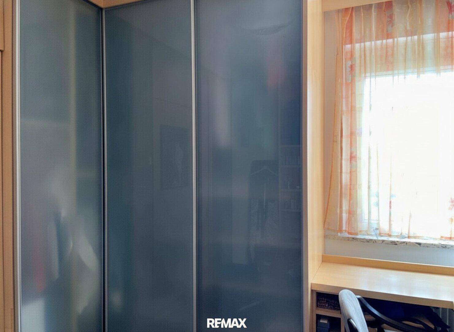 Einbauschrank mit Schiebetüren neben einem Fenster mit Vorhängen.