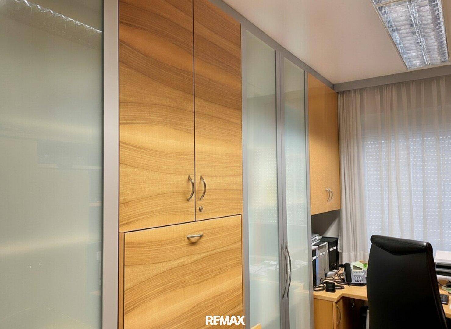Büro mit Einbauschränken, Schreibtisch und Fenster mit Jalousien.