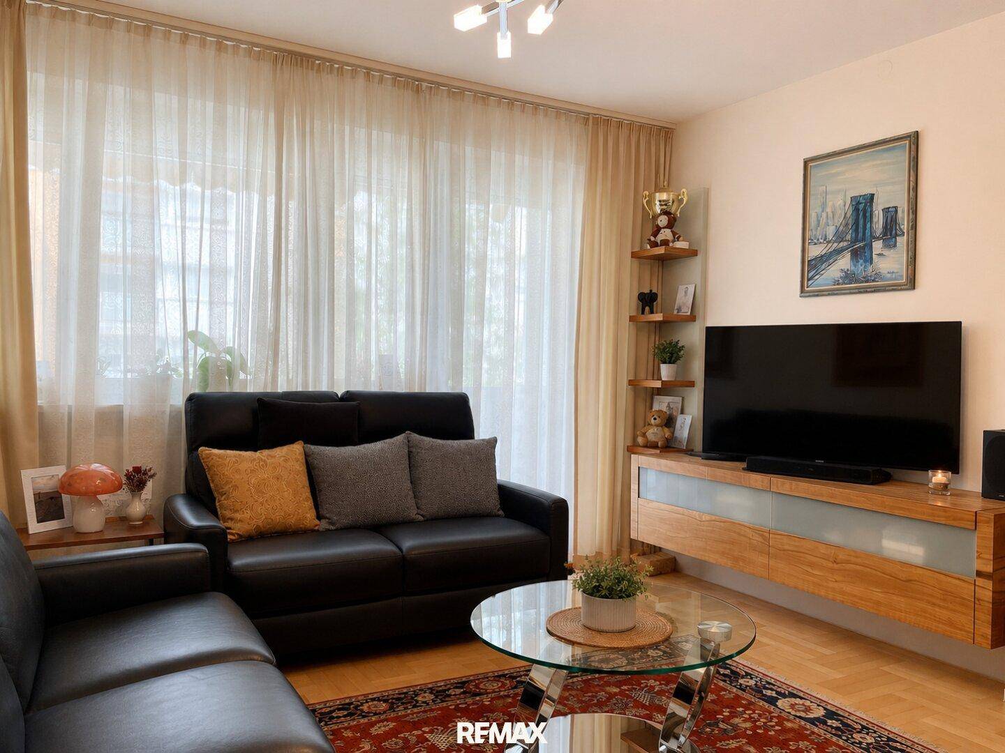 Gemütliches Wohnzimmer mit dunklen Sofas, Couchtisch und großen Fenstern für viel Licht.