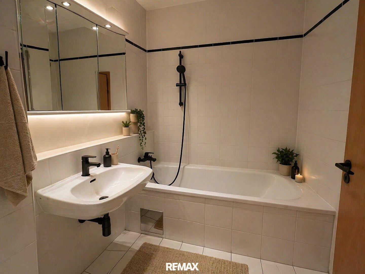 Modernisiertes Badezimmer mit Badewanne, Duschfunktion und Waschbecken mit schwarzen Armaturen.