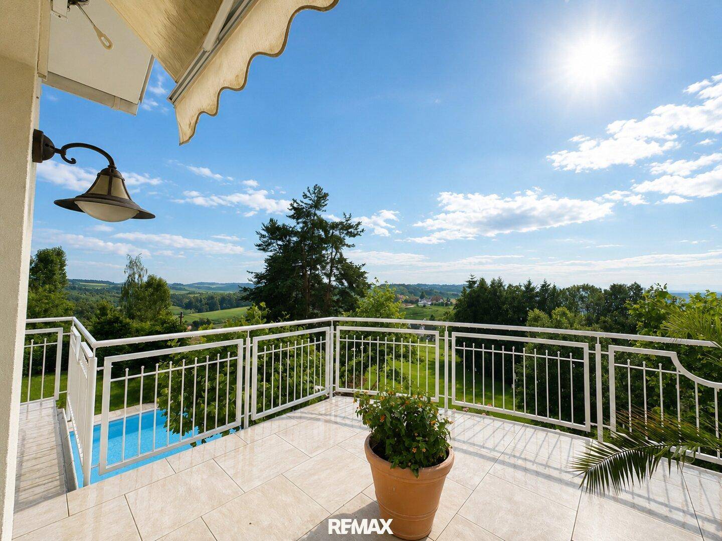 Sonniger Balkon mit Markise, Pflanzen und einem weiten Blick auf den Pool und die umliegende Natur.