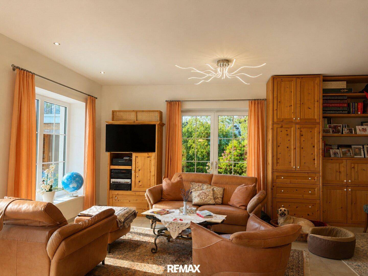 Gemütliches Wohnzimmer mit bequemen Ledersofas, Holzmöbeln und großen Fenstern zum Garten.