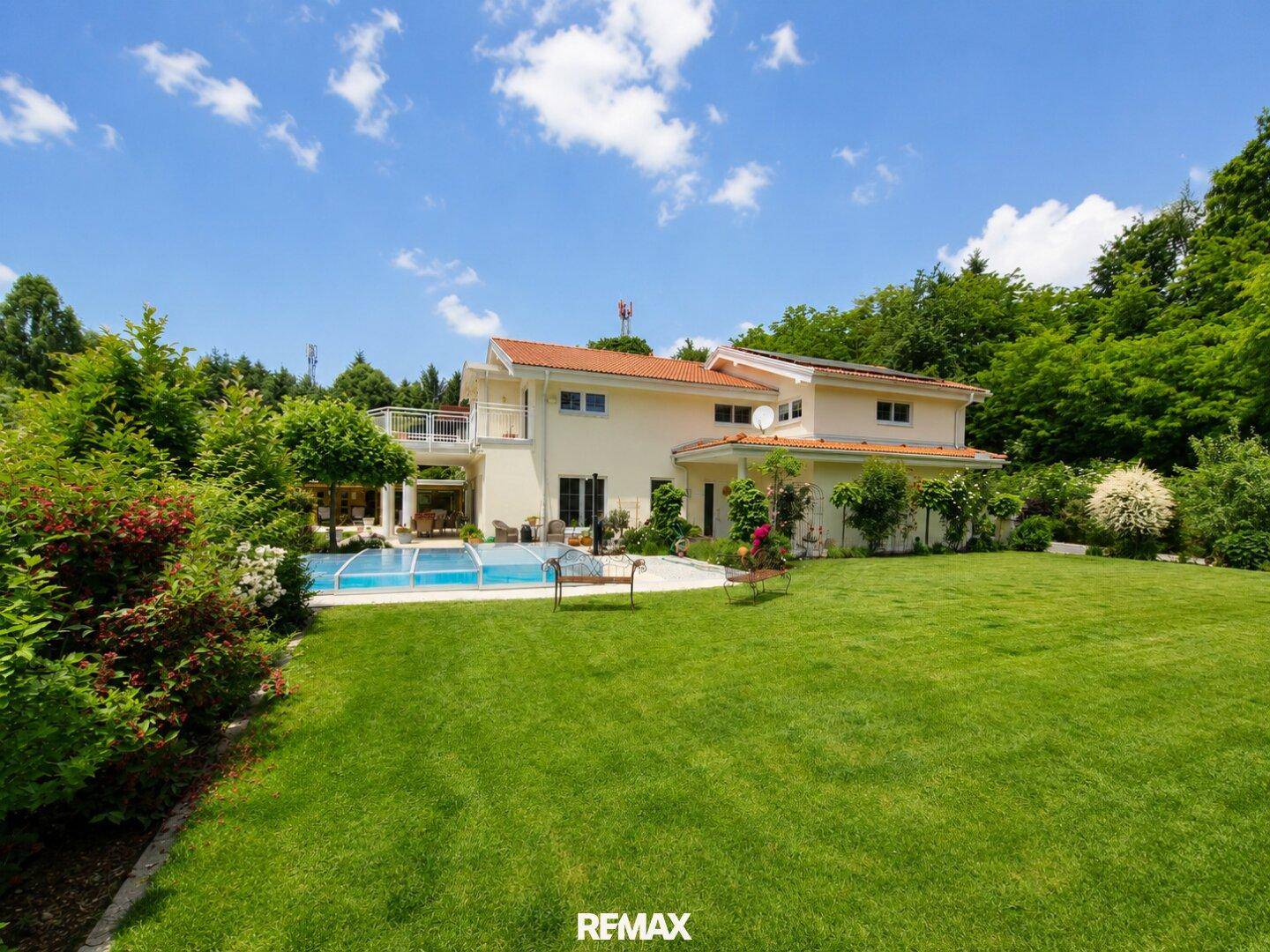 Großzügiges Einfamilienhaus mit weitläufigem Garten, Pool und umgeben von viel Grün unter blauem Himmel.