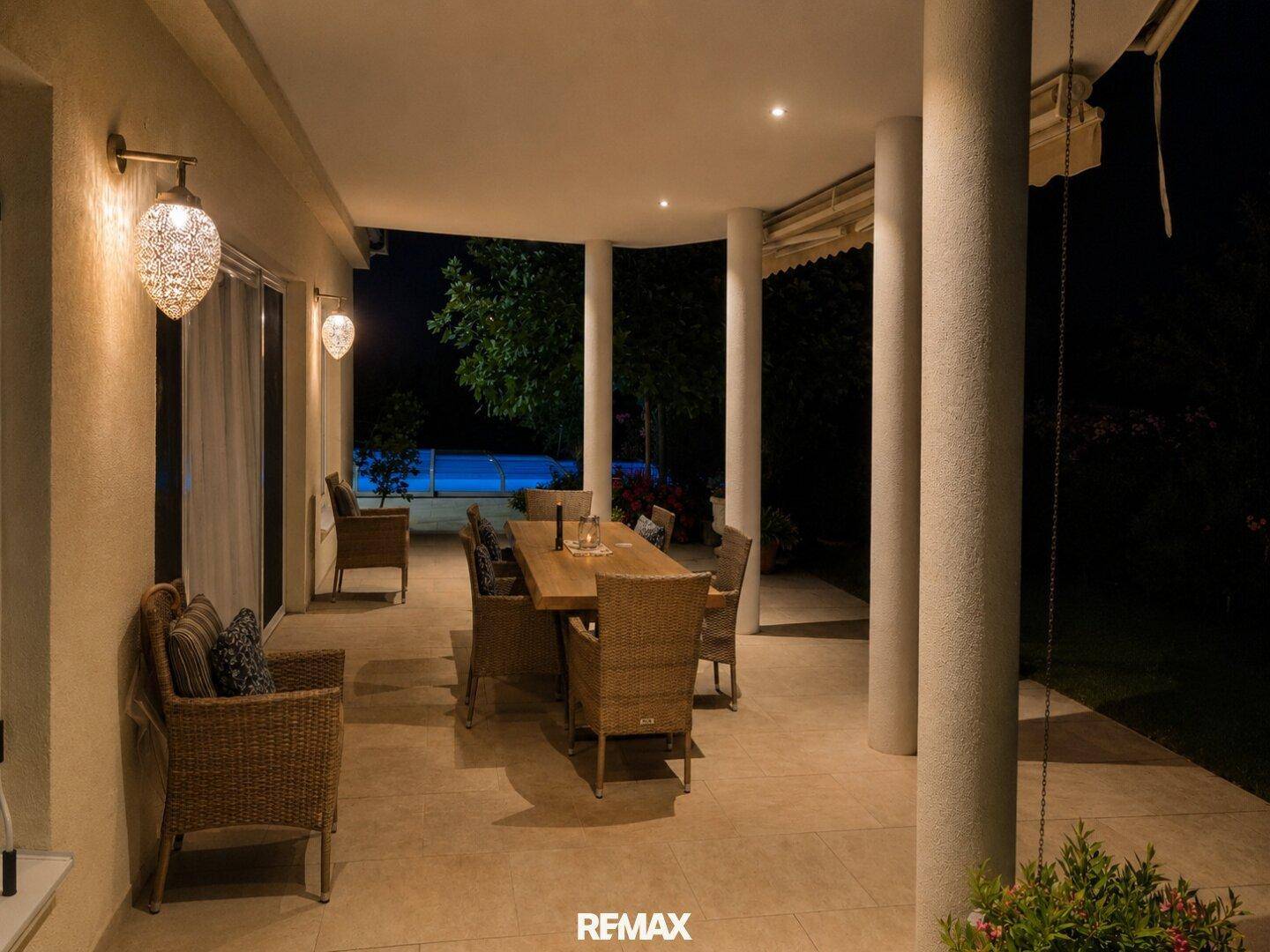 Beleuchtete überdachte Terrasse am Abend mit Rattanmöbeln und einem großen Holztisch für gesellige Stunden.
