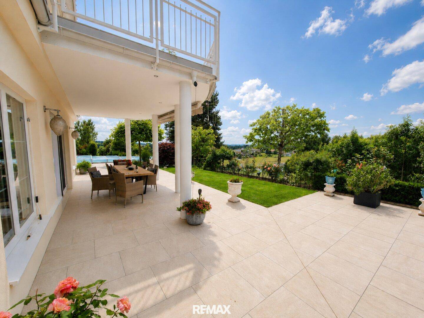 Überdachte Terrasse mit Essbereich und Blick auf den gepflegten Garten und die weite Landschaft.