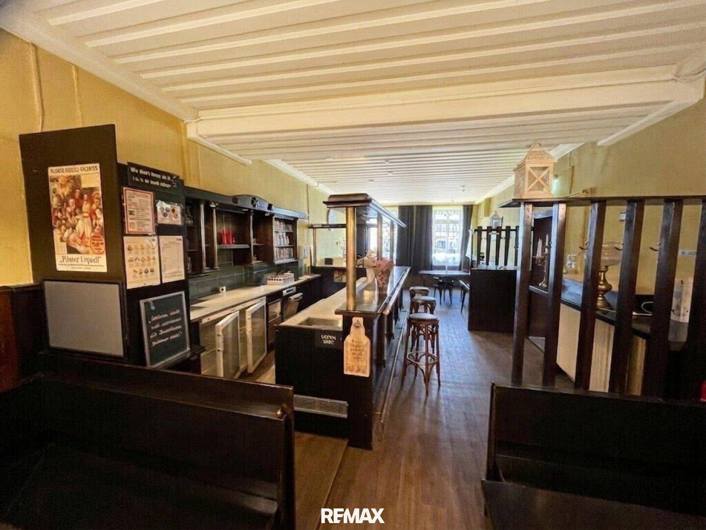 Weitläufiger Barbereich mit dunkler Holztheke, Sitzbänken und Deckenbalken in einem traditionellen Ambiente mit natürlichem Licht.