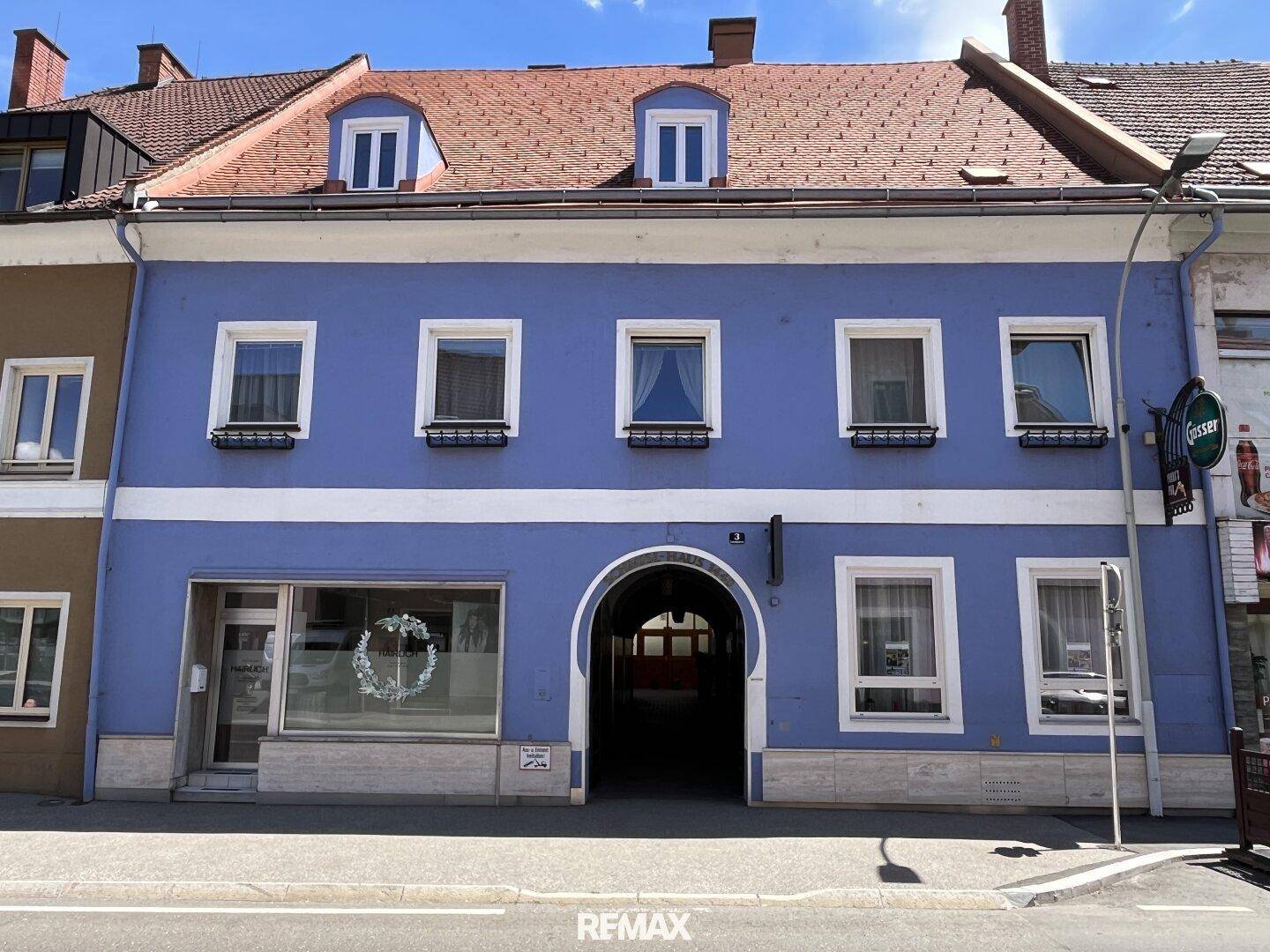 Historisches Gebäude mit blauer Fassade, roten Ziegeln und einem markanten Torbogen im Erdgeschoss an einer Straße.