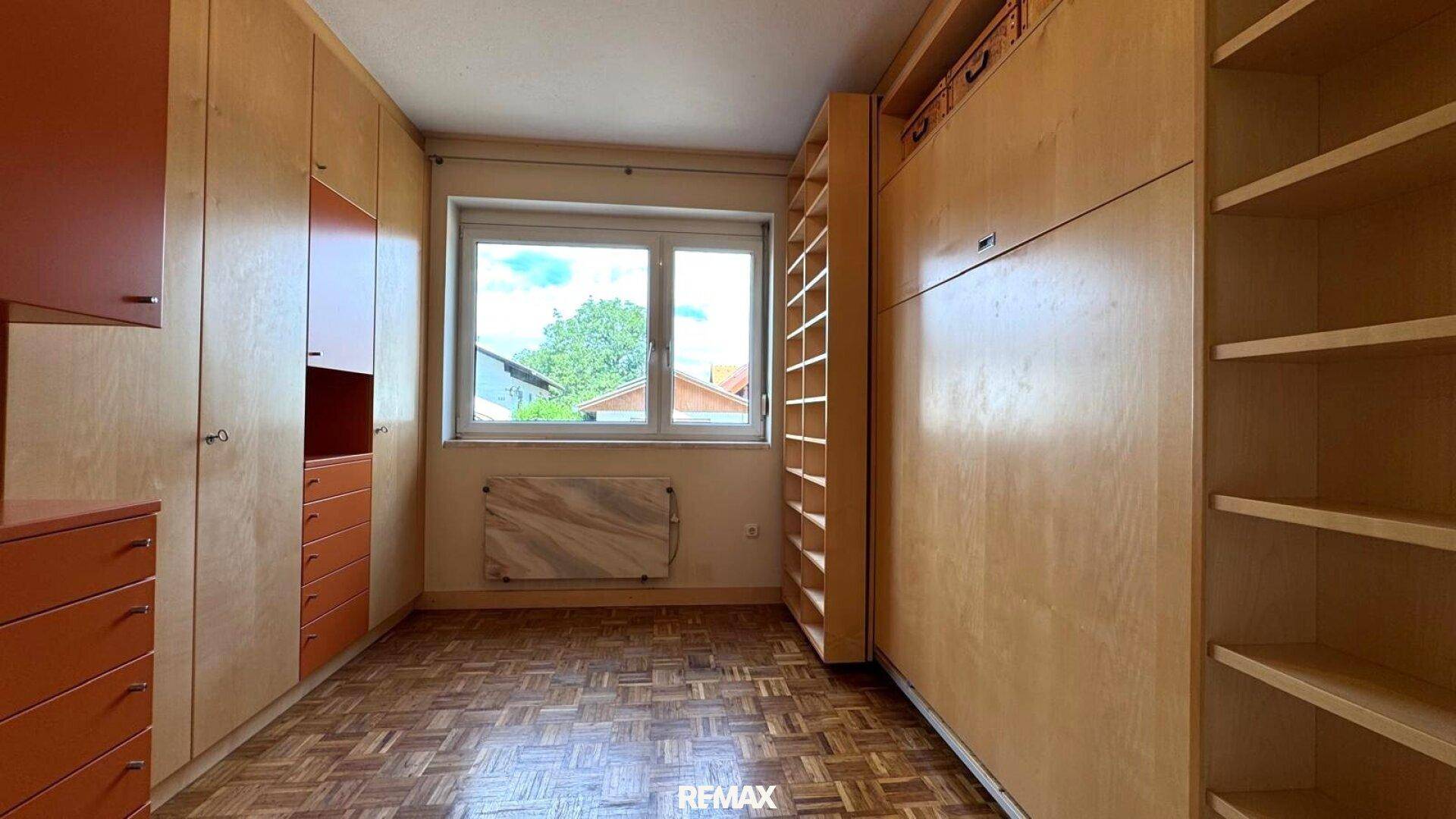 Zimmer mit vielen Einbauschränken, Parkettboden und Fenster mit Blick ins Freie.