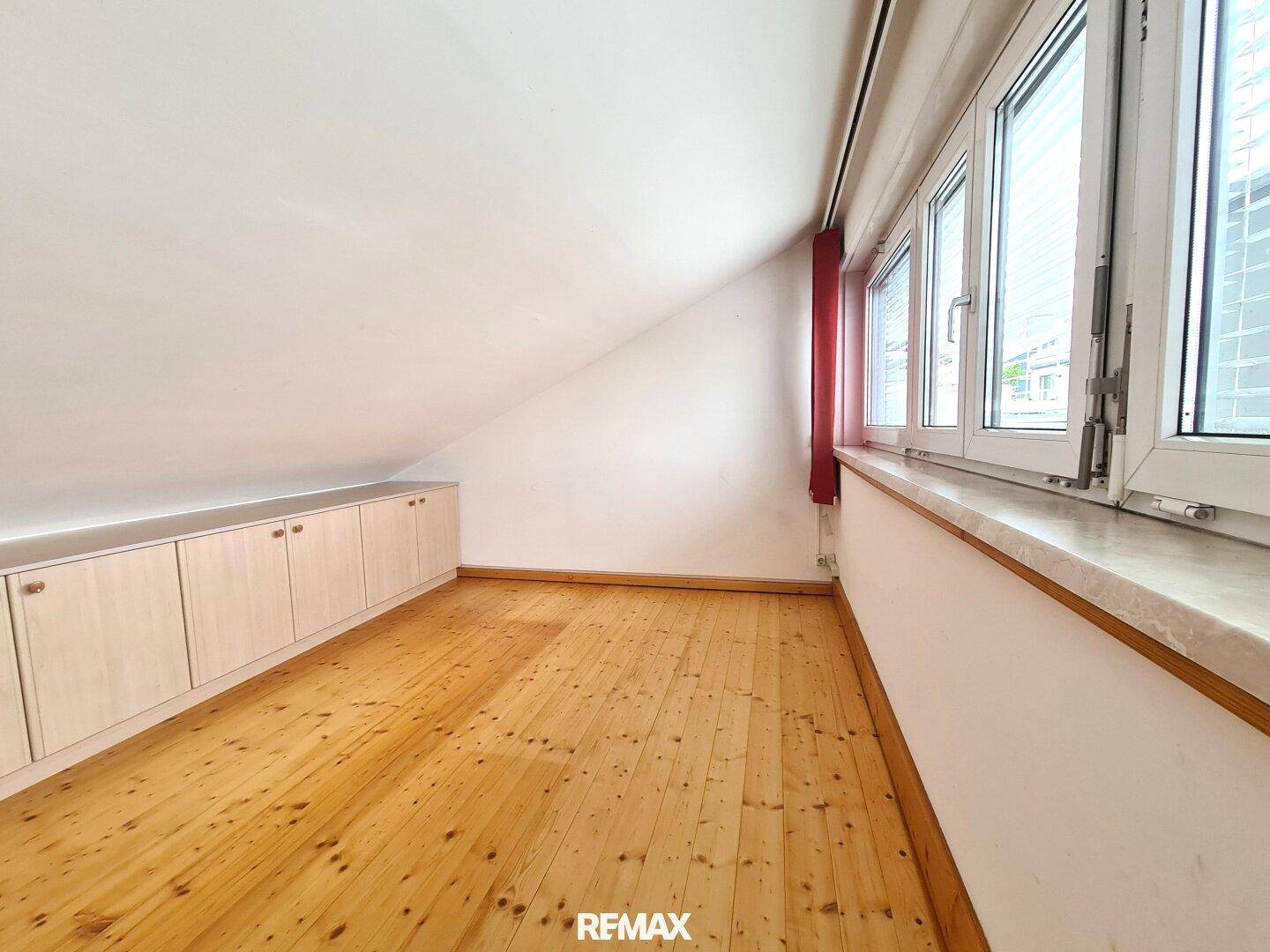 Dachzimmer mit schräger Decke, Holzdielenboden und langen Fenstern sowie niedrigen Einbauschränken.