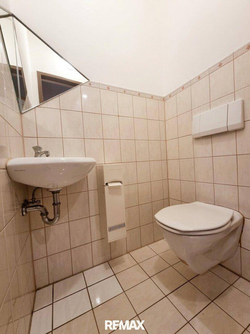 Kleines Gäste-WC mit beigefarbenen Fliesen, einem einzelnen Waschbecken und einer Wandtoilette.