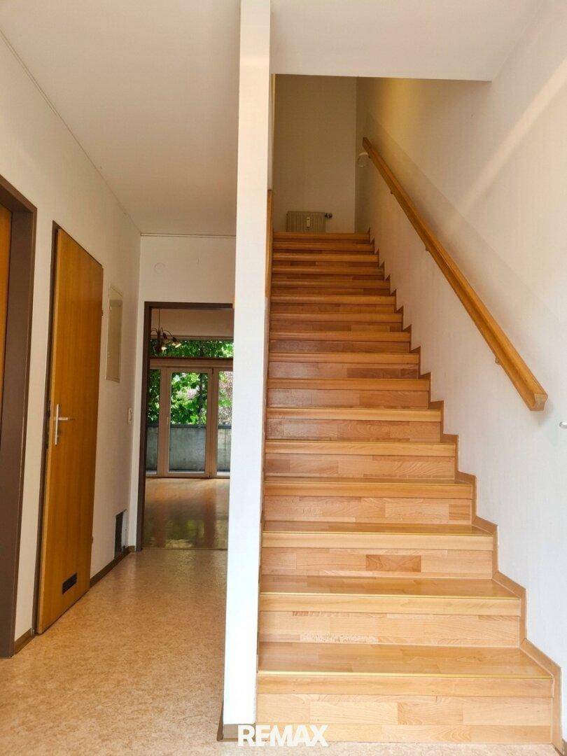 Heller Flur mit einer Holztreppe, die in die oberen Stockwerke führt, und Holztüren.