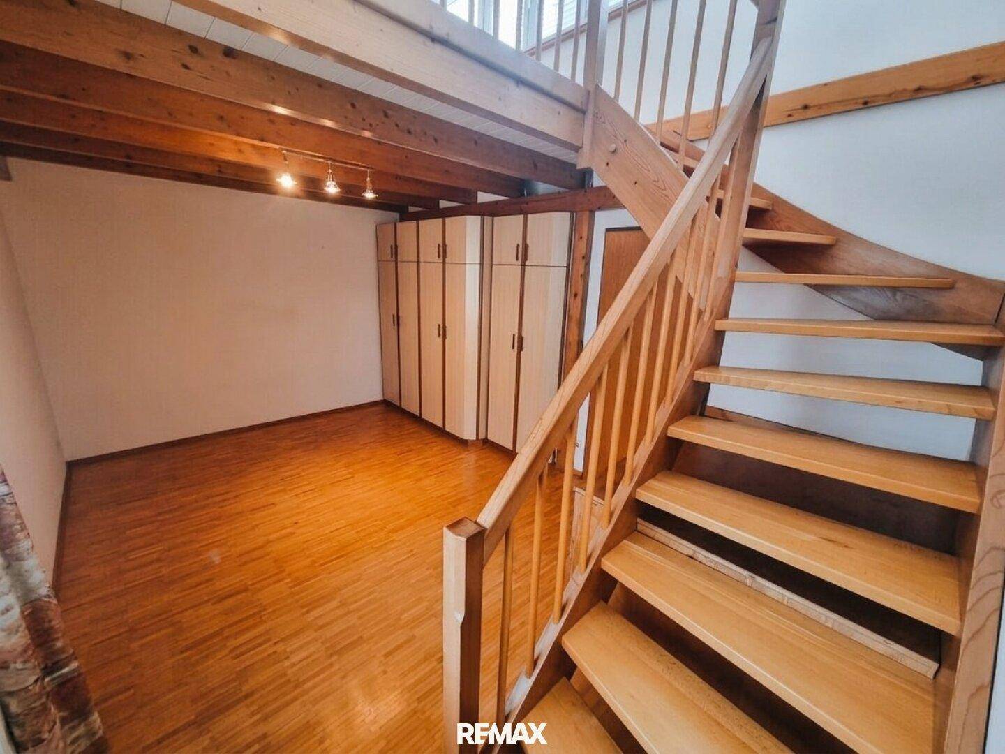 Offener Raum mit Holztreppe, sichtbaren Holzbalken und Einbauschränken, im Stil einer Maisonette.