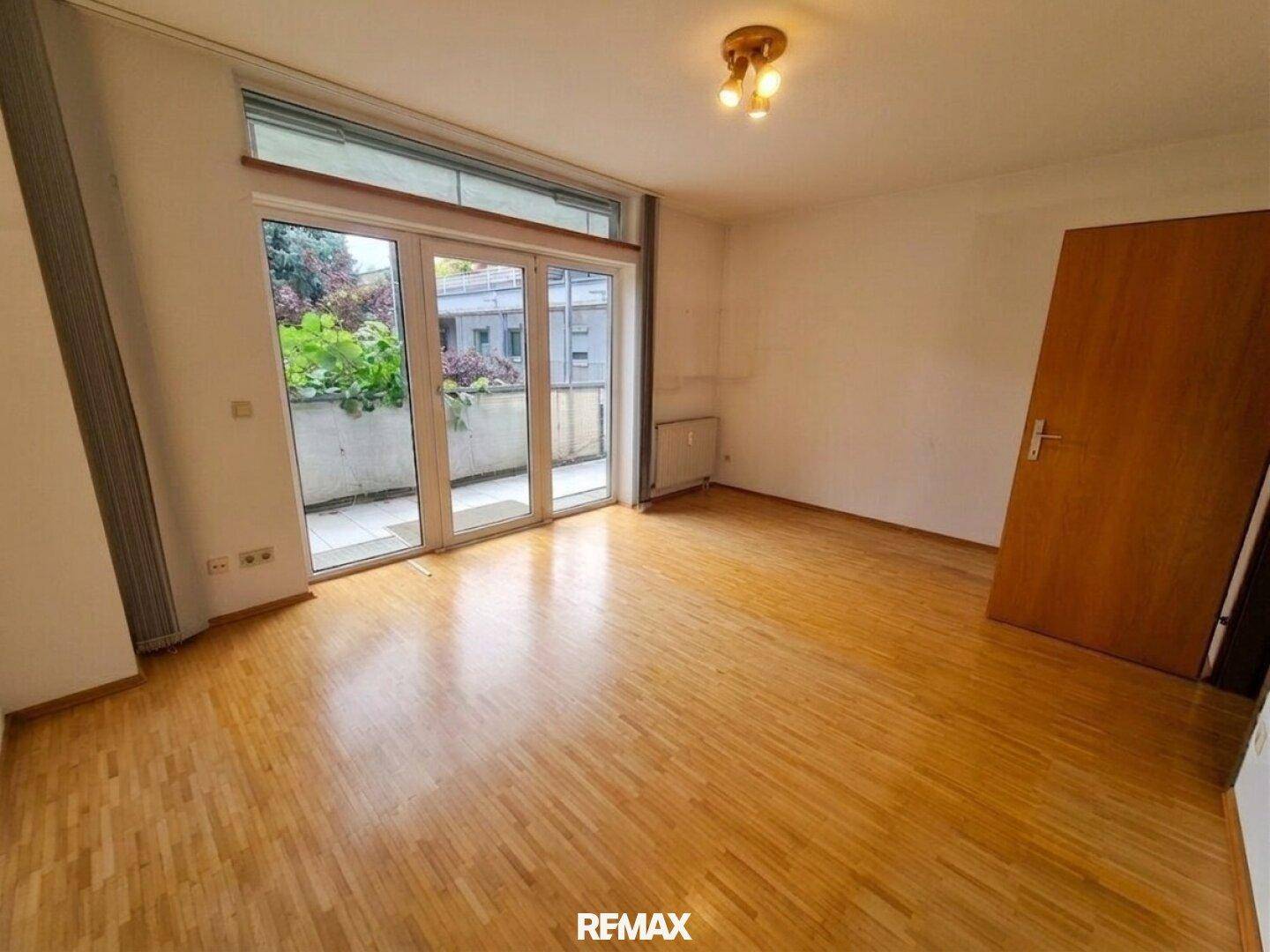 Leeres Schlafzimmer mit Parkettboden und großen Glastüren, die zu einem Balkon oder einer Terrasse führen.