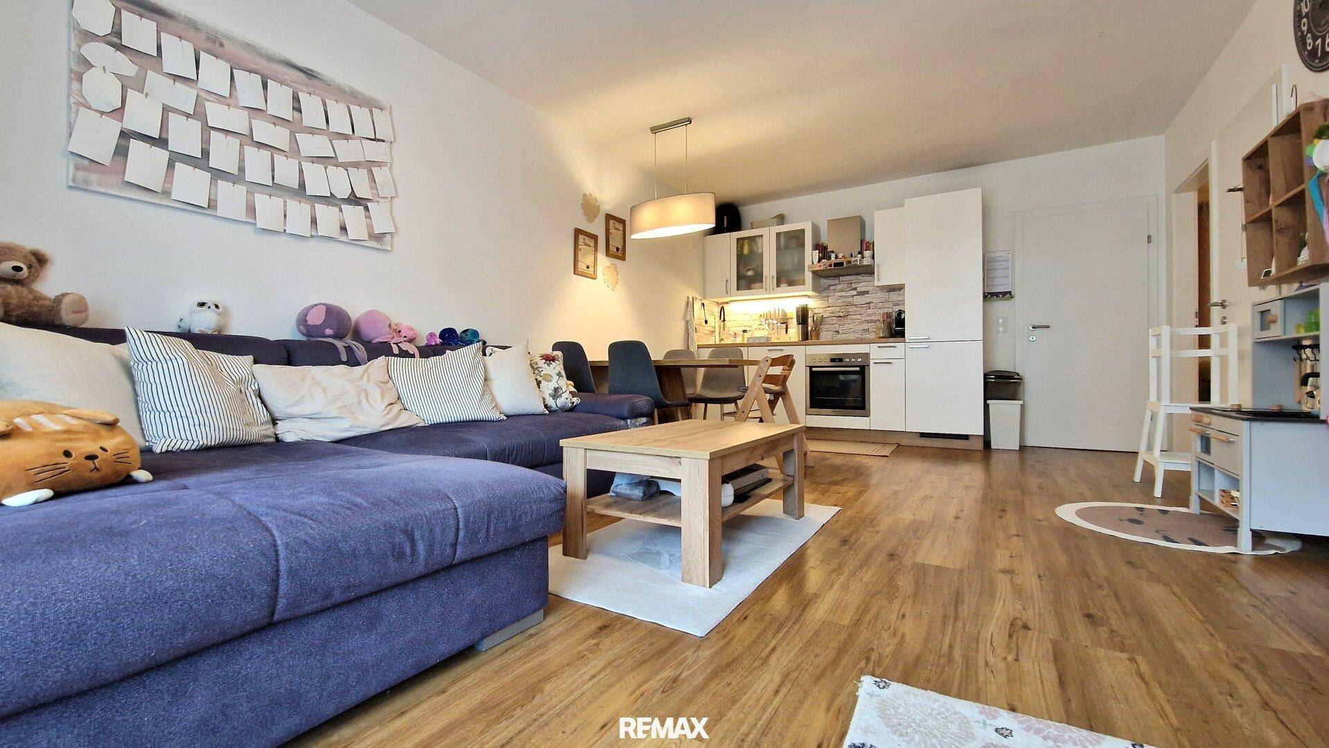 Heller Wohn- und Essbereich mit integrierter Küche und gemütlichem Sofa.