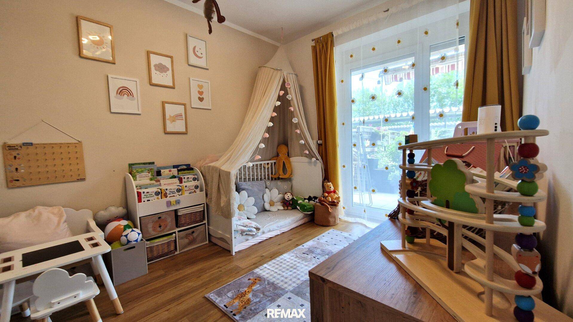 Helles Kinderzimmer mit großem Fenster, Spielzeug und gemütlichem Schlafbereich.
