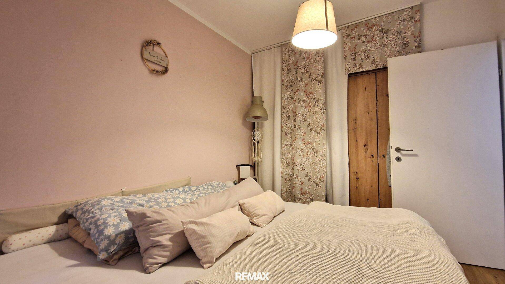 Schlafzimmer mit rosa Wänden, floraler Tapete und gemütlichem Bett.