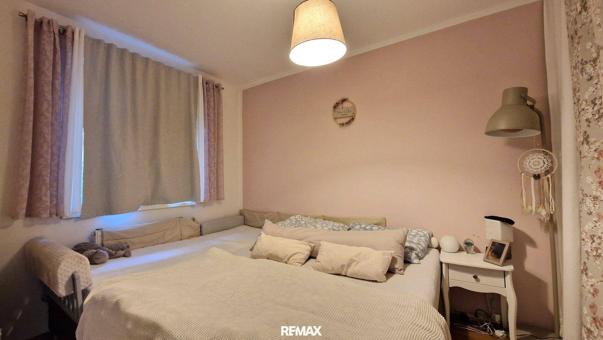 Schlafzimmer mit weichen Farben, großem Bett und Fenster mit Vorhängen.