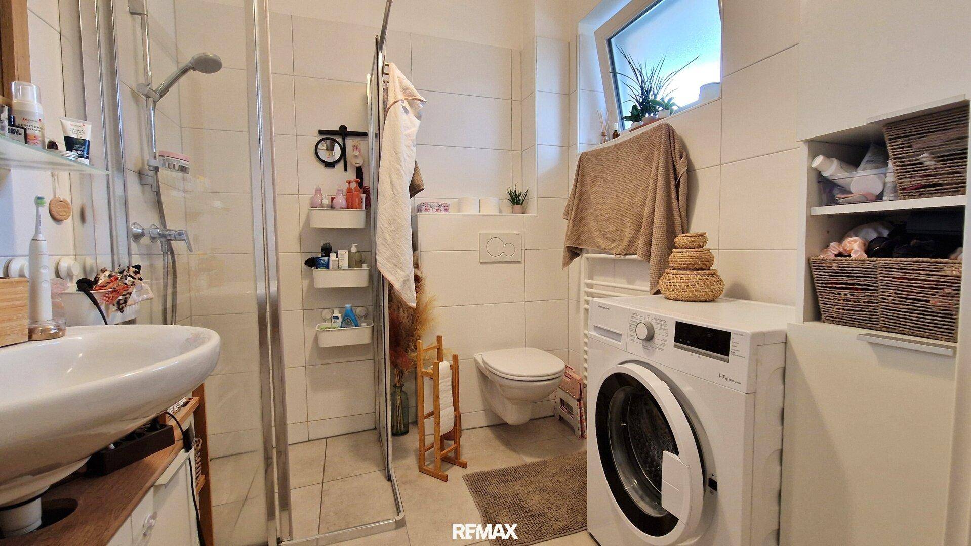 Modernes Badezimmer mit Dusche, WC, Waschmaschine und Fenster.