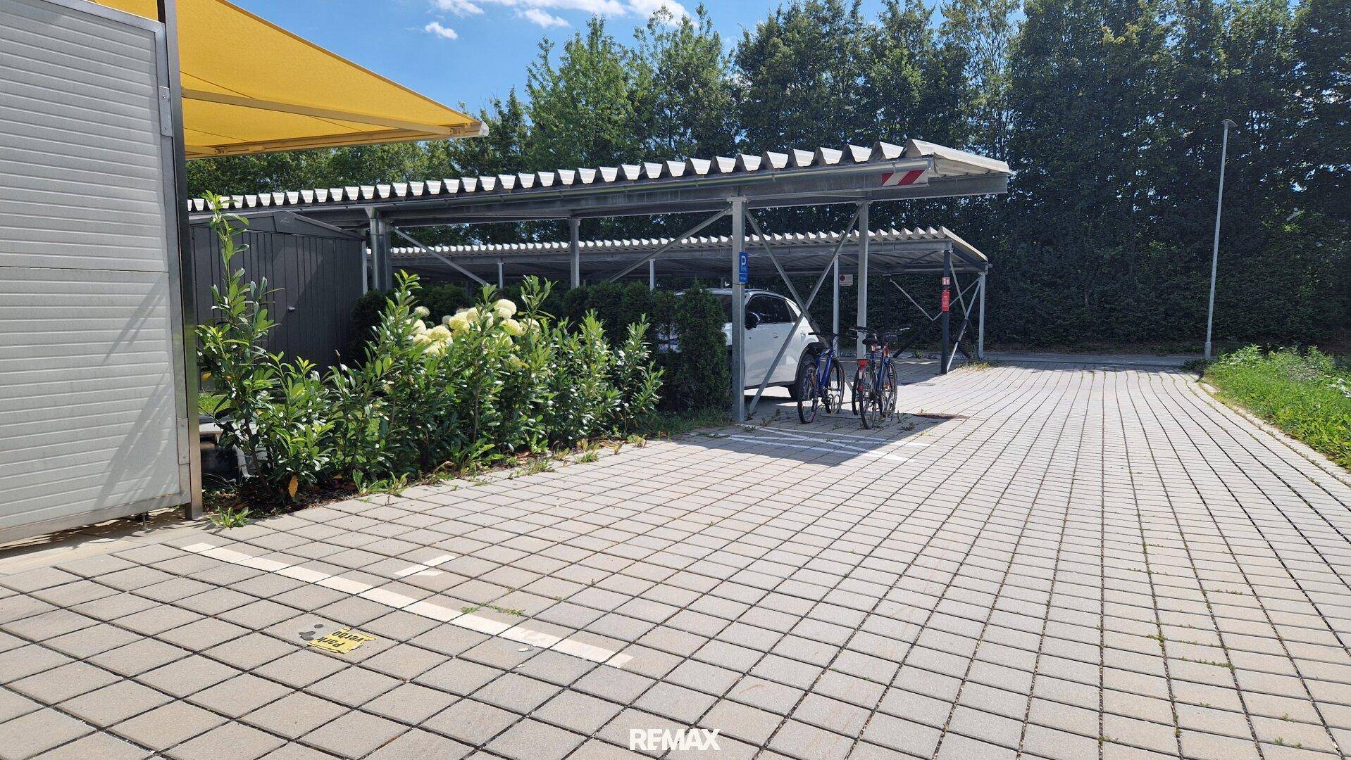 Überdachte Parkplätze mit gepflastertem Zugang und Grünflächen.