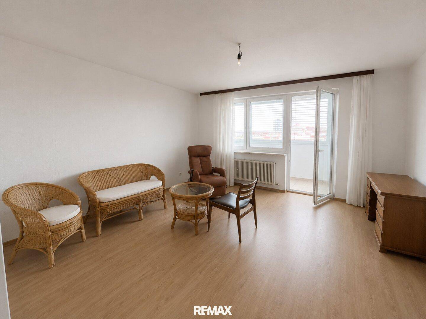 Helles Wohnzimmer mit Laminatboden, Korbmöbeln und Zugang zu einem Balkon.