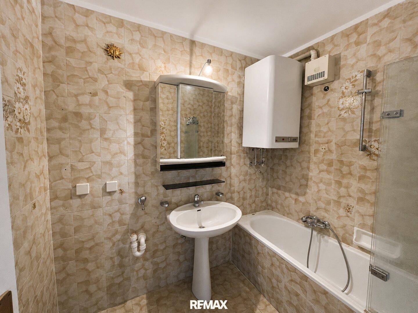 Badezimmer mit beigefarbenen Fliesen, Badewanne, Waschbecken und Spiegelschrank.