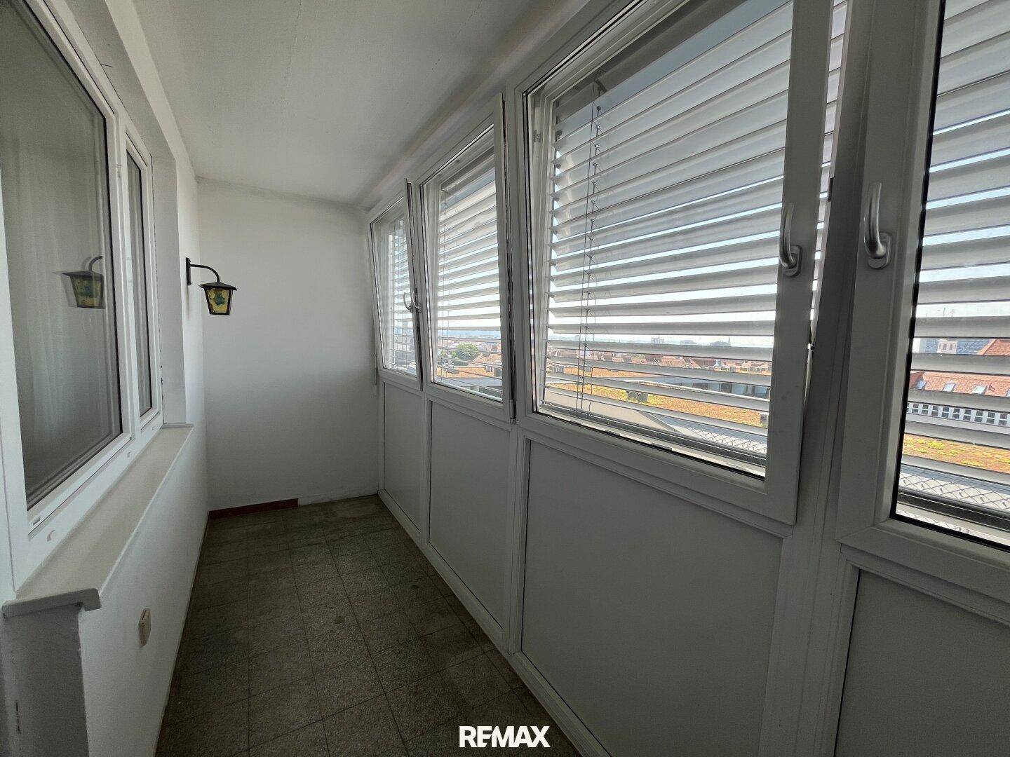 Verglaste Loggia mit Fliesenboden und Blick auf die umliegenden Gebäude.