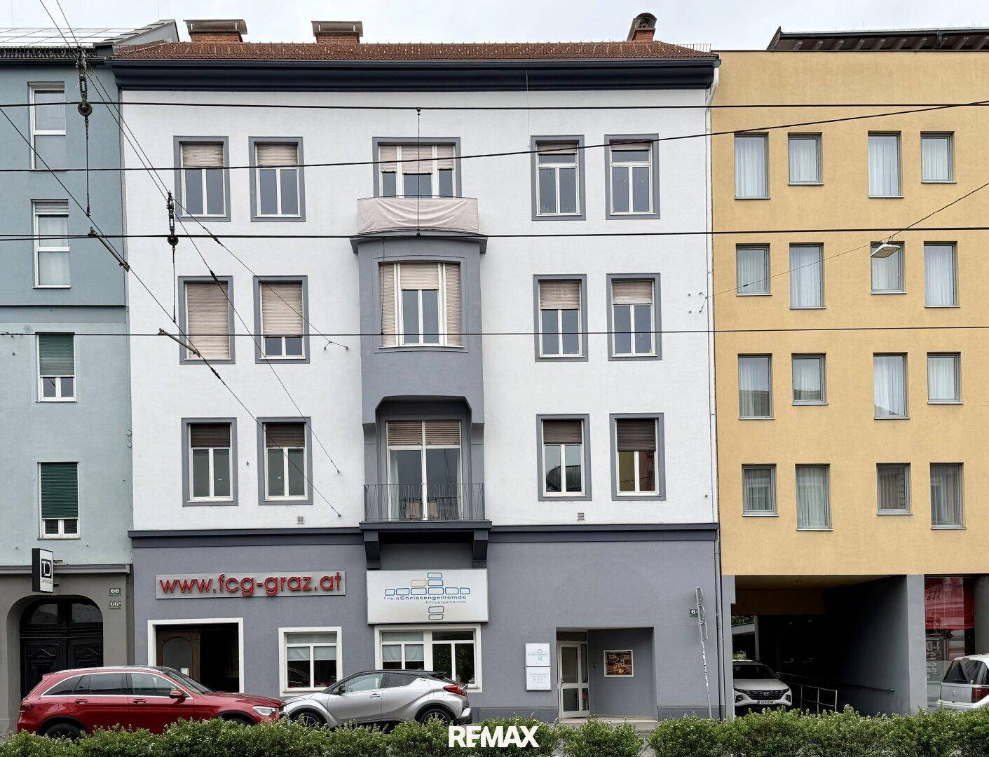 Fassade eines mehrstöckigen Gebäudes mit großen Fenstern und einem Erker, gelegen an einer Stadtstraße.