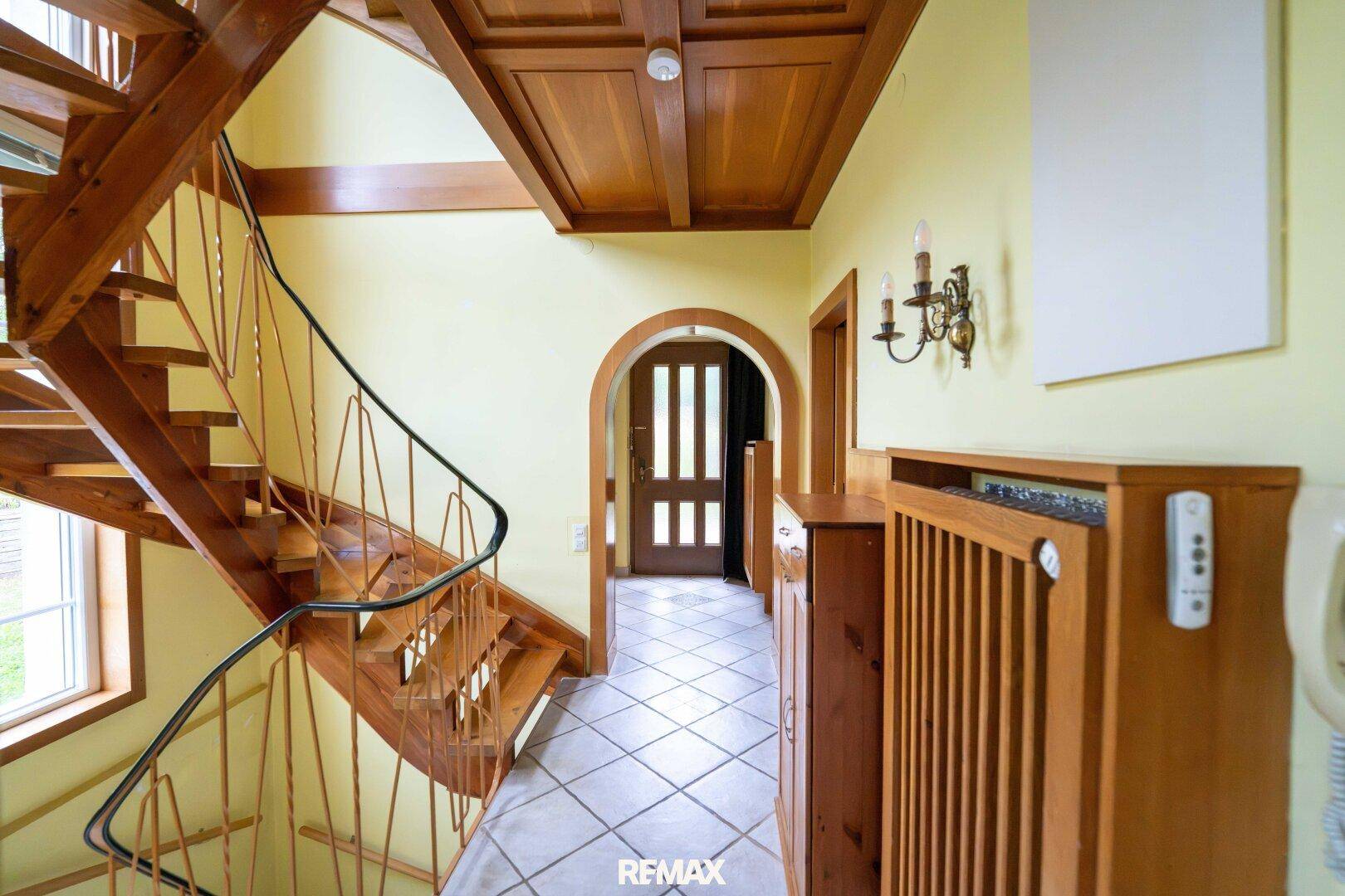 Heller Flur mit Holztreppe, gefliestem Boden und Holztäfelung an der Decke.