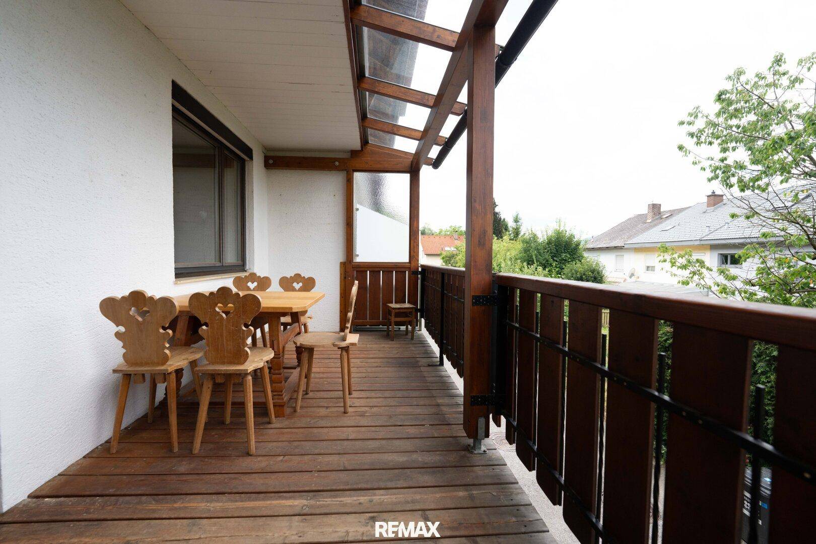 Überdachter Balkon mit Holzboden und traditionellen Holzmöbeln, ideal für Mahlzeiten im Freien.
