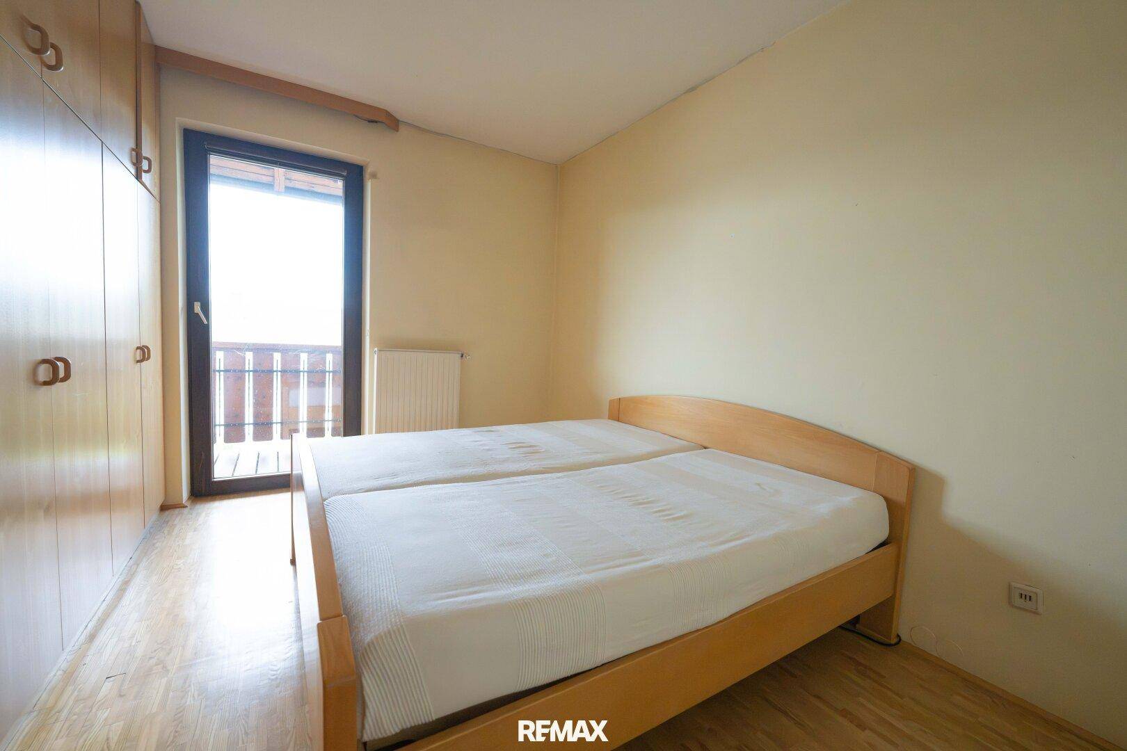 Schlafzimmer mit Holzboden, Einbauschränken und Zugang zu einem kleinen Balkon.