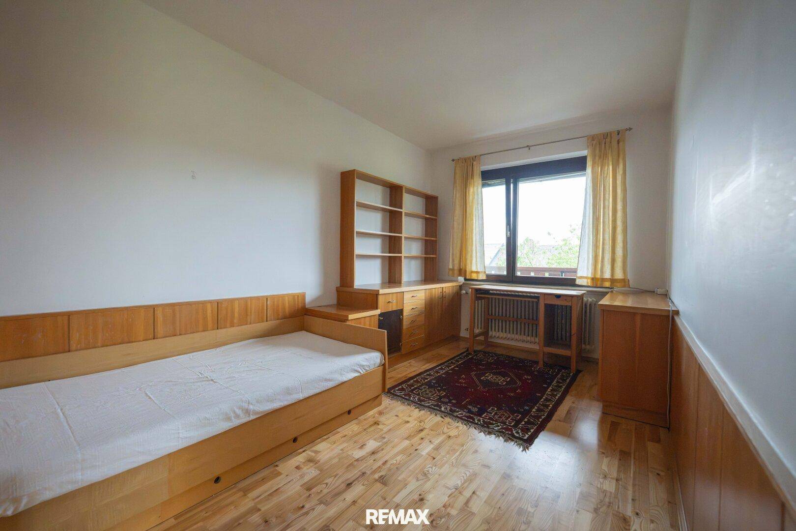 Schlafzimmer mit Holzboden, Holzmöbeln und einem Fenster mit Blick nach draußen.