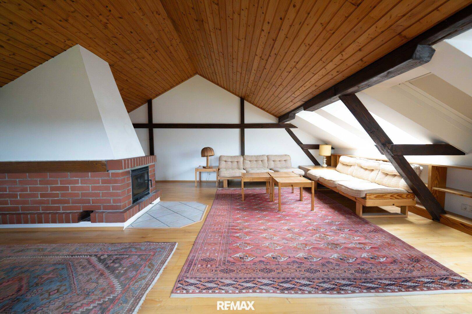 Gemütliches Dachgeschoss-Wohnzimmer mit Holzbalken, Kamin und schrägen Decken.