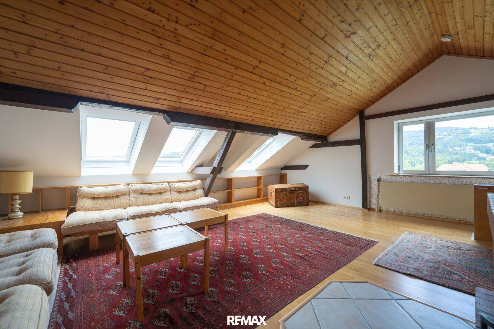Helles Dachgeschoss-Wohnzimmer mit Holzbalken, Dachfenstern und weitem Ausblick.