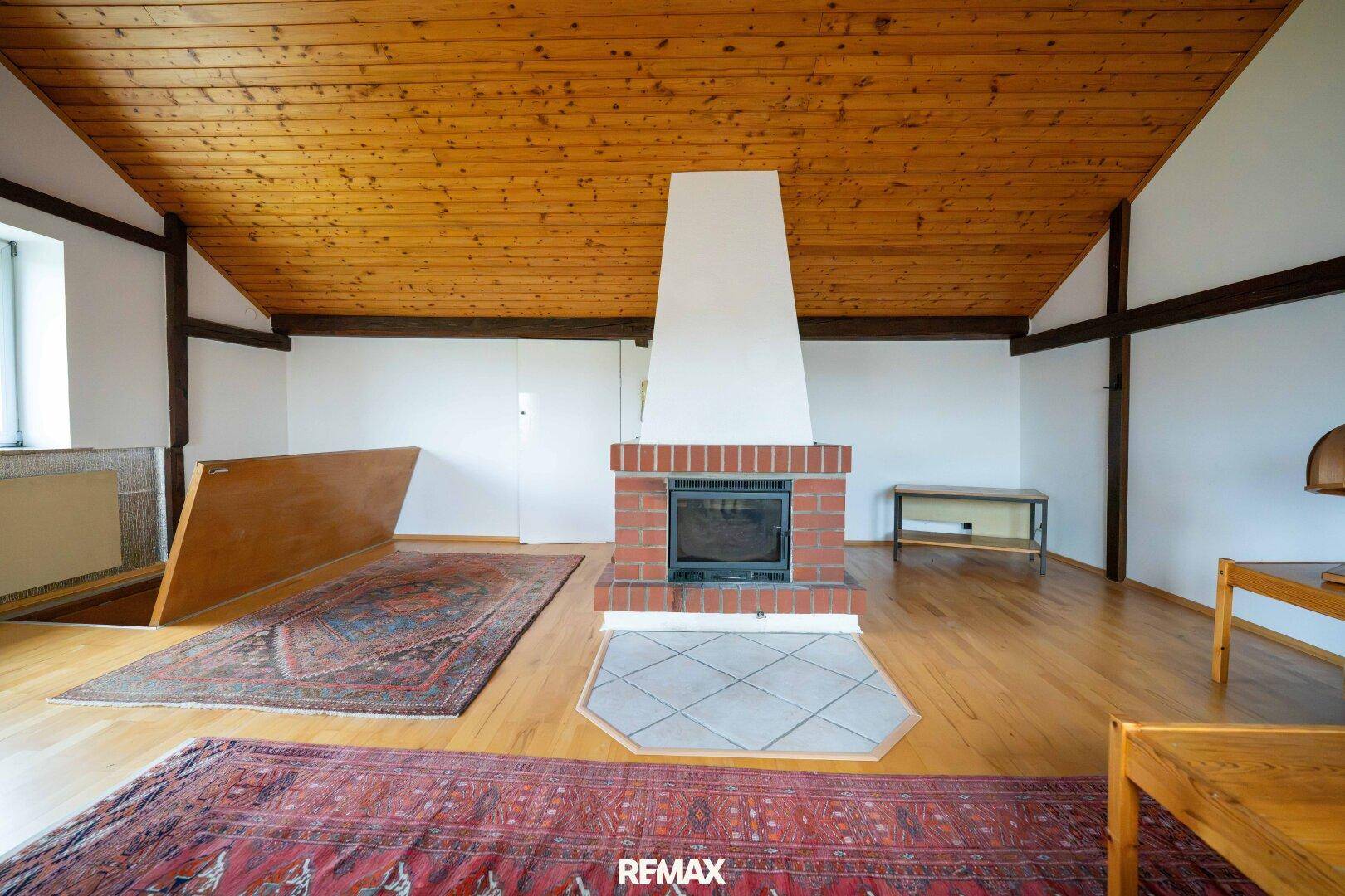 Geräumiges Dachgeschoss-Wohnzimmer mit Kamin, Holzboden und sichtbaren Dachbalken.