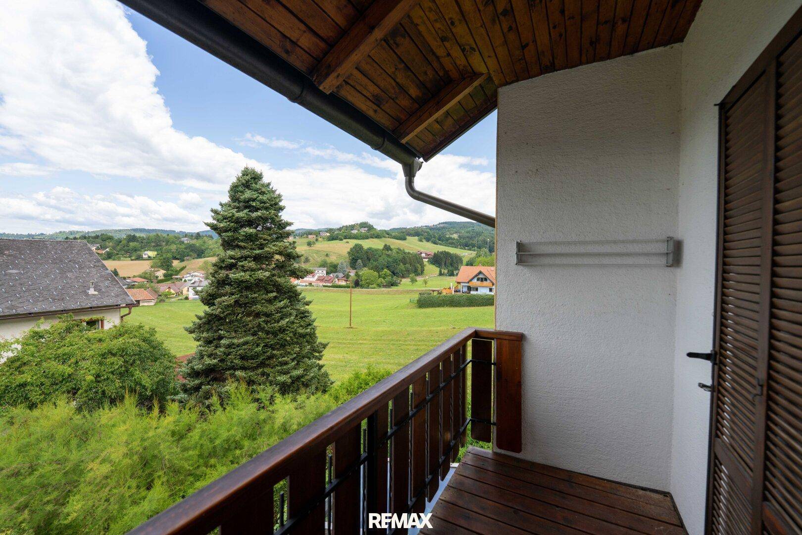 Kleiner Balkon mit Holzboden und Geländer, bietet einen weiten Blick ins Grüne.