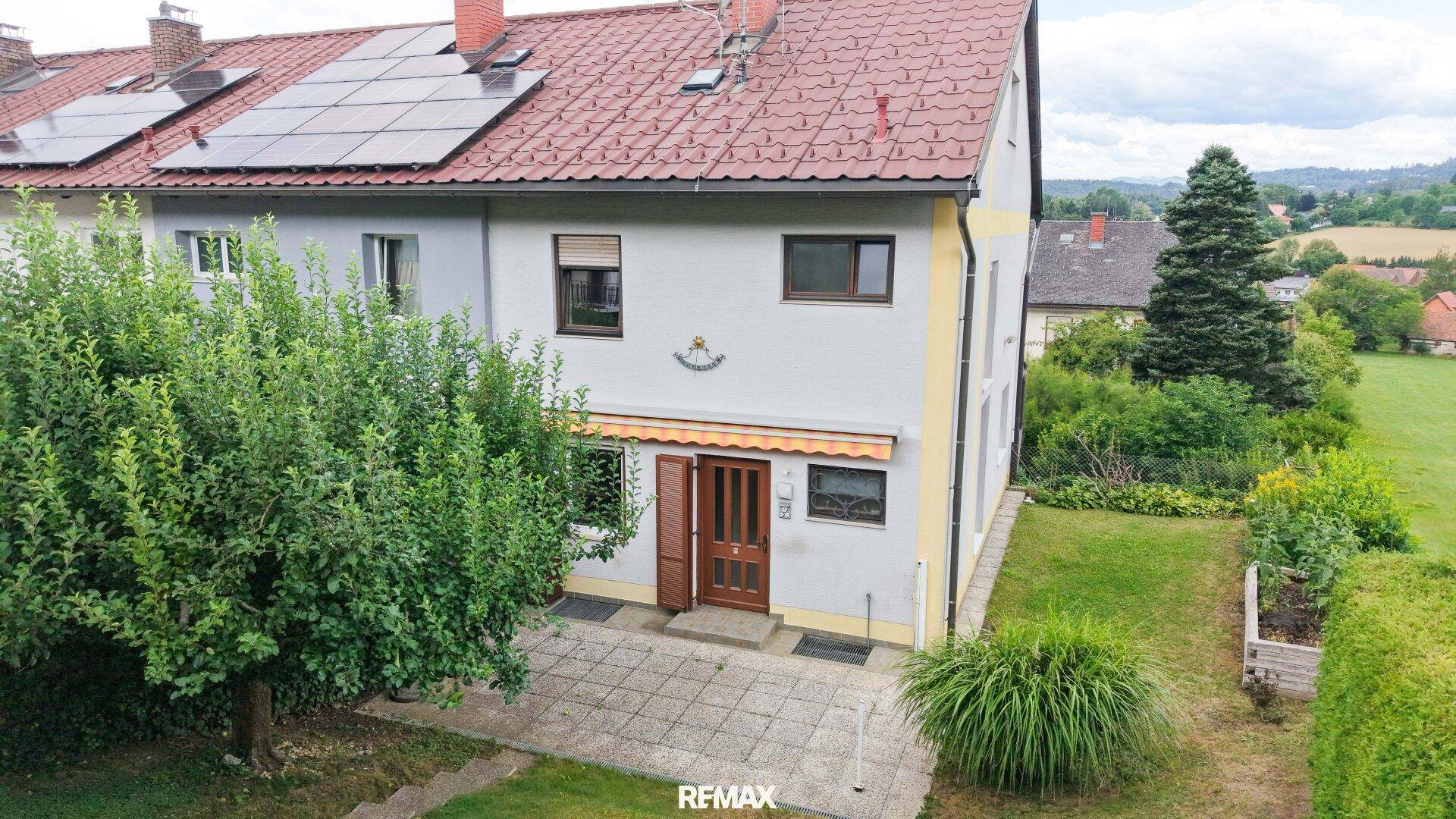 Vorderansicht des Hauses mit Garten, gepflastertem Bereich und Solarpaneelen auf dem Dach.